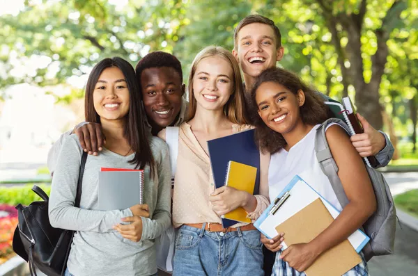 Group photo of a diverse group of students smiling in front of the school with their notebooks