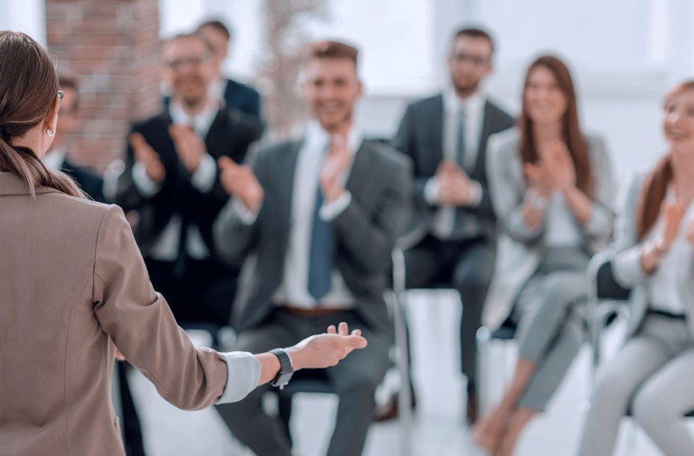 Back view of a woman wearing a jacket giving a speech to an audience