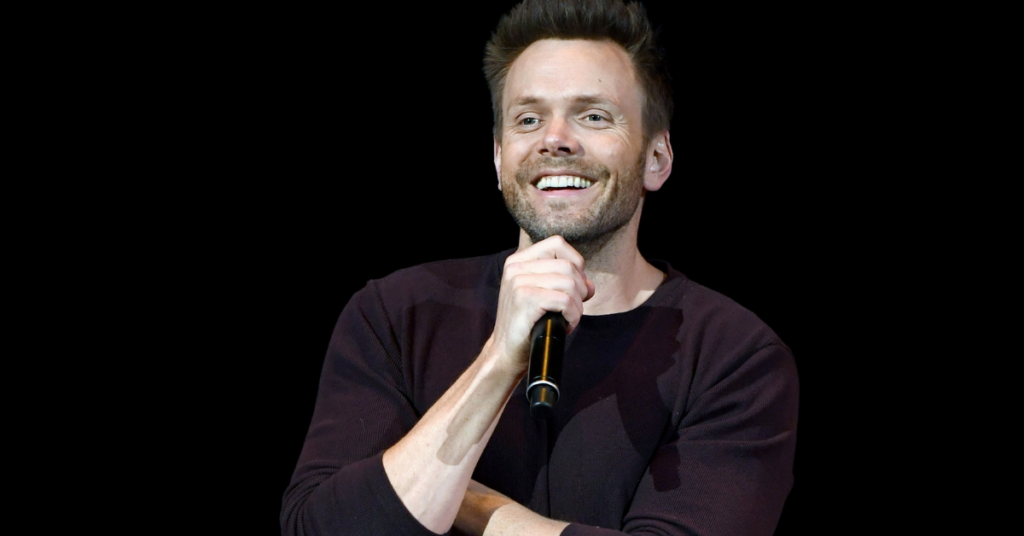 Joel McHale onstage smiling with mic in hand