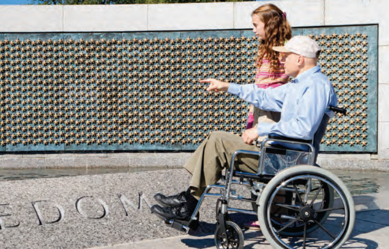 veteran in wheelchair visiting memorial with granddaughter