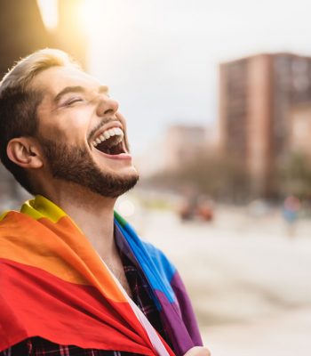 A man is wearing a rainbow flag and laughing